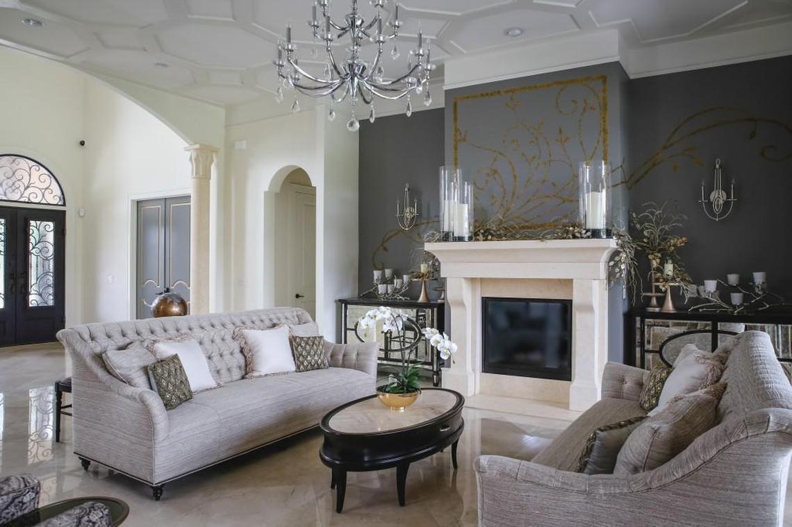 Custom hand painted artwork and florals glitter on the fireplace wall (Sherwin-Williams Classic French Gray). The burnished buff Crema Marfil marble floors, columns and fireplace add to the grandeur, with the stunning ceiling detail and chandelier completing the room’s elegant look.