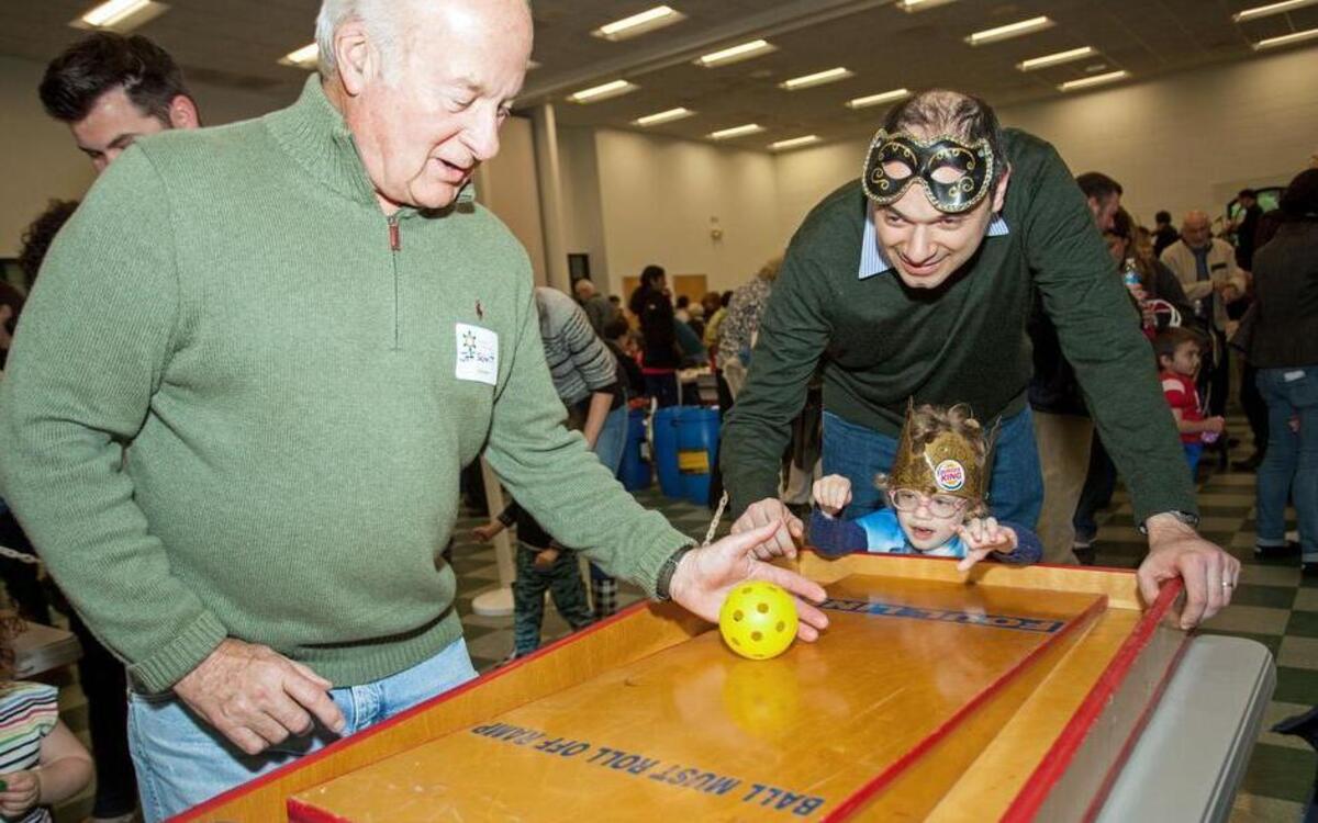 Abby Freidman rolls a ball up a ramp at a game station as her father, Eugene, top right, and volunteer Jeff Schmitt assist during a community celebration of the Jewish festival Purim, at the Cary Senior Center at Bond Park in Cary, N.C. on Sunday, March 20, 2016.