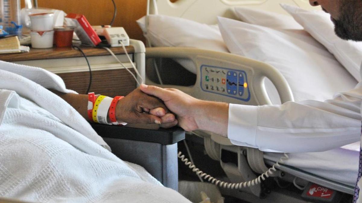 Duke Raleigh Hospital Chaplain Adrian Dixon, right, holds a patient’s hand during prayer on a recent Friday morning.