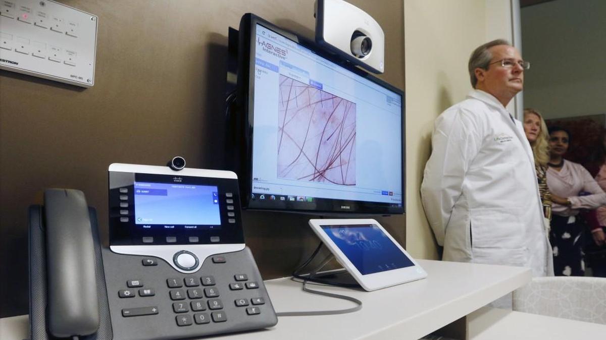 
Dr. Craig Warner, medical director of the new 7,000 square foot Cisco LifeConnections Health Center listens to questions about the telemedicine capabilities, left, for patients interviewing in Exam Room #9 during the grand opening tour by guests Wednesday.
