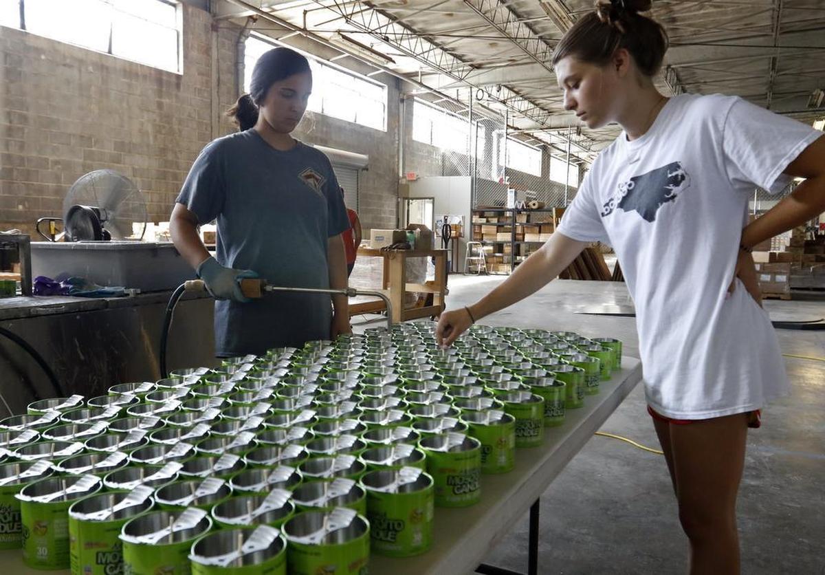 Krista Gilbert, left, fills nine-ounce cans of Murphy’s Naturals while fellow employee Audrey Hammerstein straightens the wicks in each can July 28 at Loading Dock, a new co-working space in Raleigh.