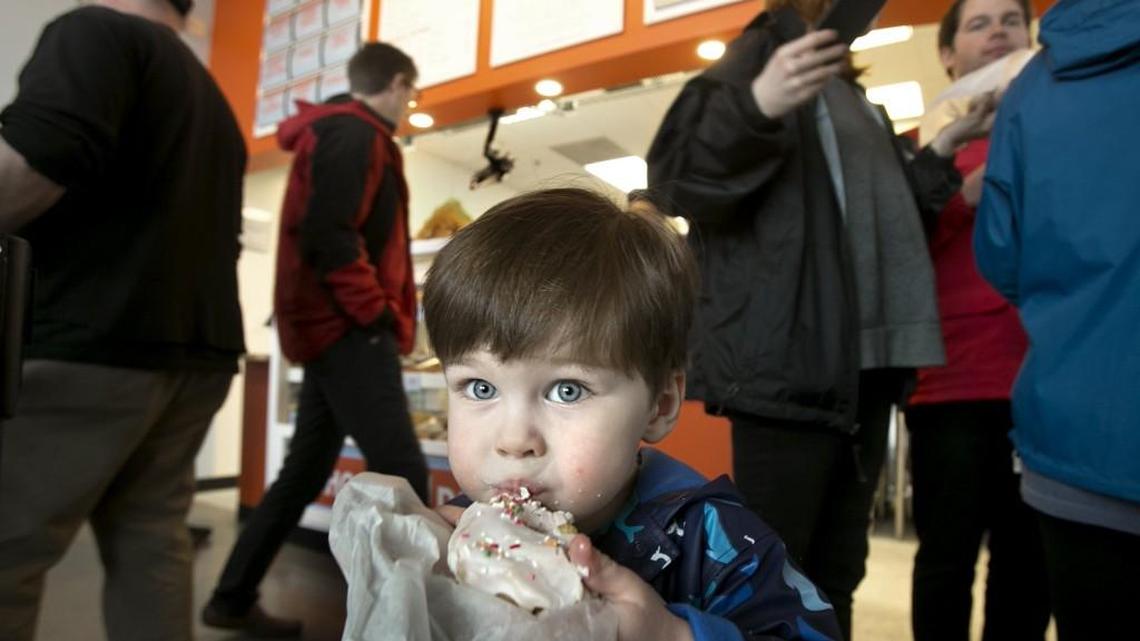 Patrons, like Ross Mize, 2, of Chapel Hill, gets his first taste of a Rise donut who lined up around the building in light rain for their first tastes of donuts at a free giveaway at Rise-Carrboro on Tuesday, February 23, 2016 from 12-2pm.