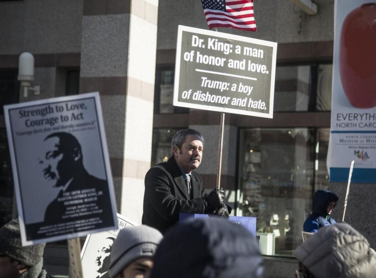 Michael Lindsay of Raleigh, center, holds a sign with his thoughts about Martin Luther King Jr. and President Donald Trump prior to a march in honor of King Monday morning, Jan. 15, 2018 in downtown Raleigh during the annual MLK Memorial Day March.