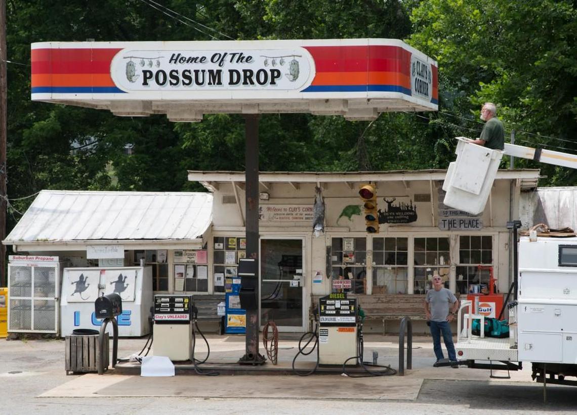A photo of Clay’s Corner in Brasstown, N.C. The small family-owned gas station and convenience store, now closed, was home to the annual Possum Drop on New Year’s Eve, during which locals celebrate the New Year with the lowering of a live opossum. Clay Logan, in green, uses friend Bob Byers’ truck to hang a sign on Tuesday, July 8, 2014.