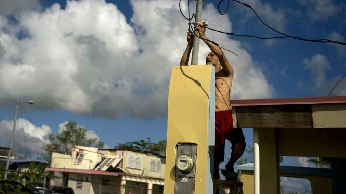 In this Friday, Oct. 13, 2017 photo, a resident tries to connect electrical lines downed by Hurricane Maria in preparation for when electricity is restored in Toa Baja, Puerto Rico. A month after the storm rolled across the center of Puerto Rico, power is still out for the vast majority.