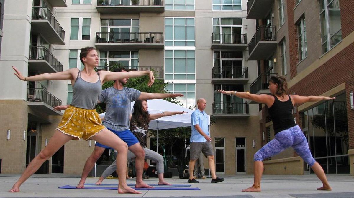 At right, Jesalyn Keziah leads her pop-up yoga group on the plaza at 140 West Franklin as a passerby walks through on Thursday, Sept. 22, 2016, in downtown Chapel Hill, NC. Keziah was invited to the plaza as part of events being held during the Chapel Hill Farmer’s Market.