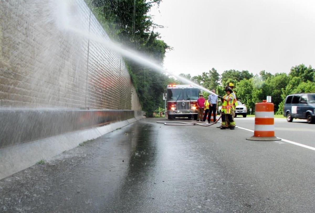 Carrboro firefighters Kassandra Kreplak and Chris Covington wash down a portion of the concrete retaining wall along the N.C. 54 off-ramp at Jones Ferry Road, while Carrboro Alderman Damon Seils and project manager Michael Adamson watch. The mural – about 9 feet tall at its highest point and 75 feet wide – is being paid for with an $8,000 grant from Carrboro Tourism Development Authority. Artist Michael Brown will start painting Wednesday, July 13, 2016, and take about a month to complete the work.