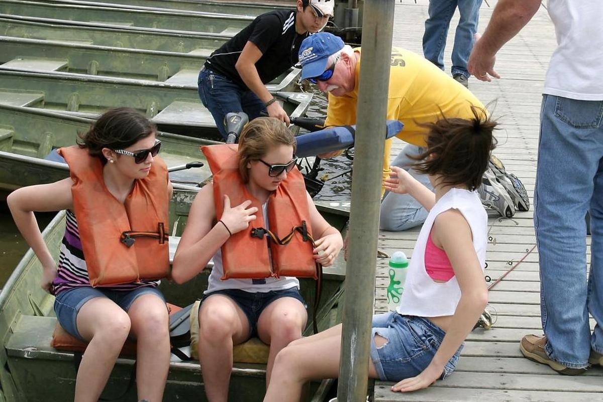 From left, Grayson Carey and Joleigh Duty sit in a boat as Sophie Carey boards and boathouse workers help steady the vessel at the Lake Benson dock in 2014.