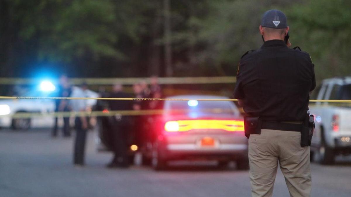 An armed security guard surveys the murder scene at a parking lot at the Bay Creek Apartments complex on Hudson Avenue at twilight Wednesday.