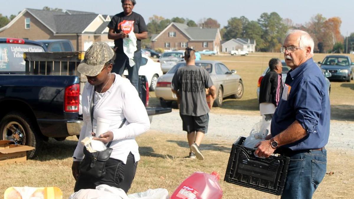 Volunteers and clients of Angels On A Mission food ministry carry boxes of food, bags of sweet potatoes and other items to cars parked outside Lighthouse Christian Fellowship on N.C. 210.