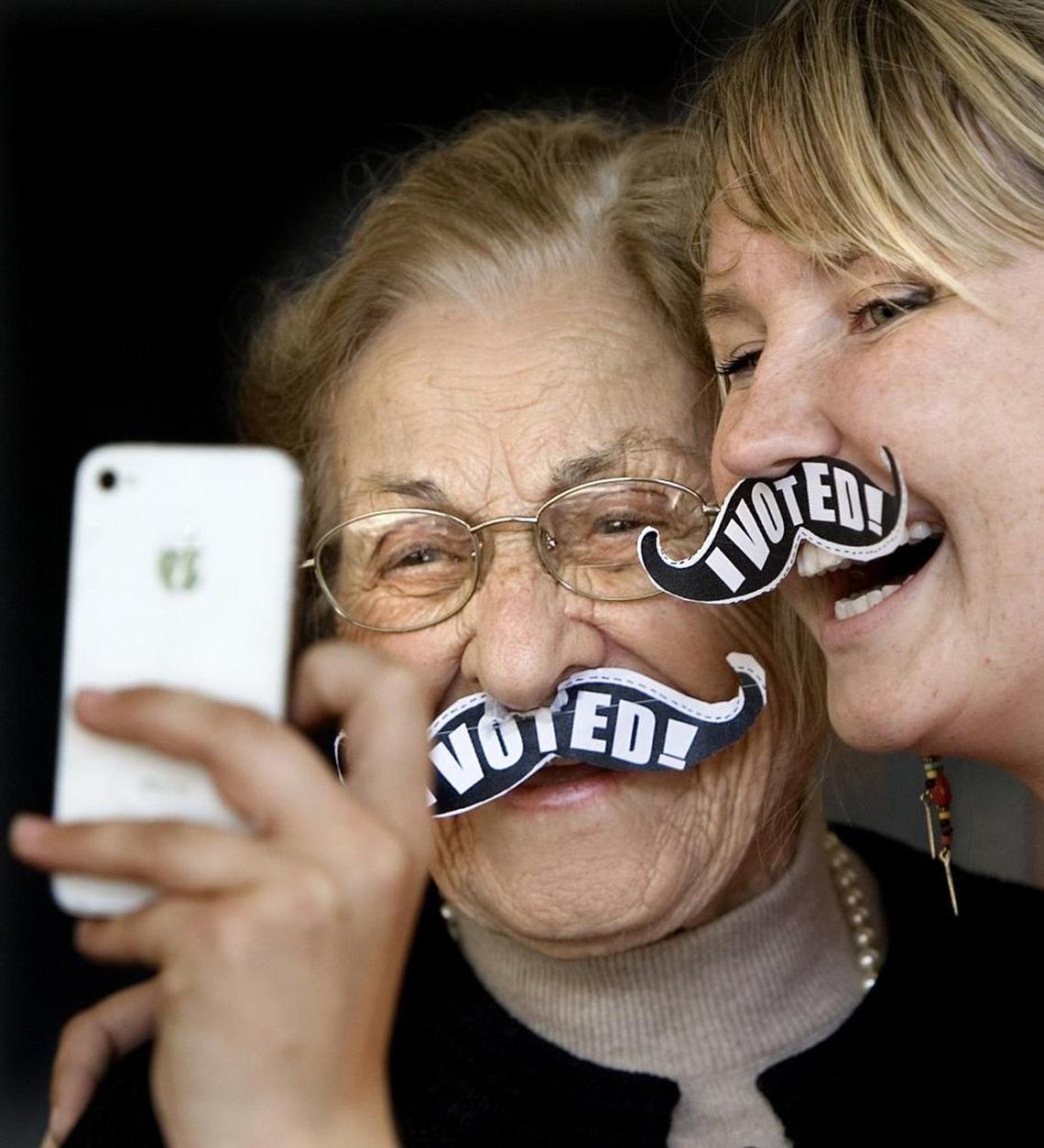 Pota Vallas, 104, of Raleigh, left, has her iPhone photo made with Irene Cadwell, 27, of Raleigh, the new voters project campus organizer with NCPIRG (North Carolina Public Interest Research Group) on Thursday, October 18, 2012 in front of the Talley Student Center on N.C. State University's campus. Vallas, who has voted in every small and major election since coming to the country from Greece in 1924, also wanted to sport a paper mustache. The group was distributing on the first day of early voting. In addition, they were hoping to get a one-day goal of 4,000 students willing to pledge to vote across 5 state campuses. Their longer-term goal is to get 100,000 student pledges before the November national election by continuing to being present on campuses.