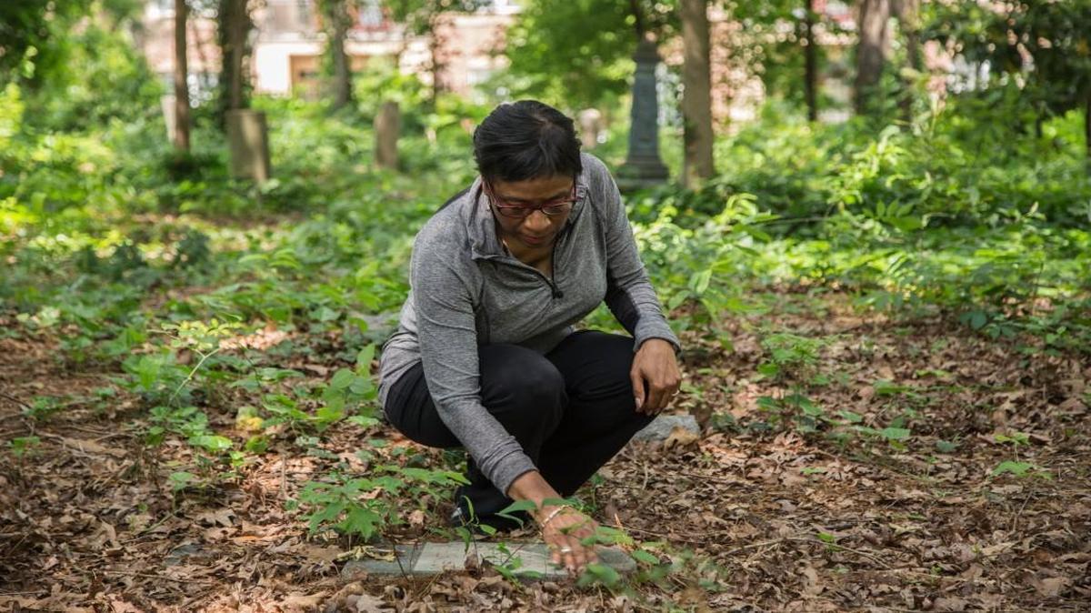 Sabrina Goode, who is descended from an early settler in Oberlin Village where many freedmen bought land and settled after the Civil War, clears debris from a grave stone at her family's burial plot at the three-acre Oberlin Cemetery near Cameron Village in Raleigh. Goode is a volunteer who has worked to care for Oberlin Cemetery, where there may be as many as 600 graves.