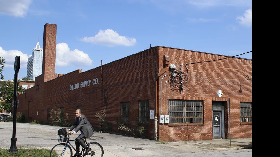 
A cyclist rides past the Dillion Supply Warehouse in Raleigh’s warehouse district. Kane Realty seeks rezonning that would allow for a 18-story office tower on the southern end of the property currently occupied by a two-story Dillon Supply warehouse. The company hopes to preserve as much of the 67,000-square-foot warehouse as possible. 
