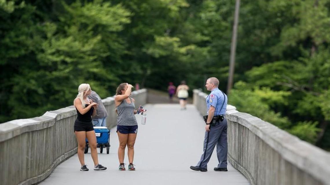 A Raleigh police officer talks with Lake Johnson visitors on the pedestrian bridge at the popular city park on Monday morning July 17, 2017, in Raleigh, N.C. Police were searching the park after a report of an assault on one of the trails Monday morning.