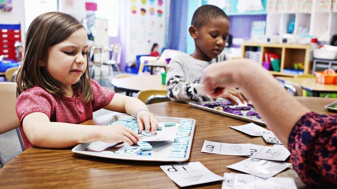 Kindergartener Ellaree Belford makes a face as she sounds out a word while working with classmate Noah Smith, center, and instructional assistant Deborah Chapman, right, at Powell Elementary School in Raleigh on Jan. 5, 2017. Critics worry that state legislative efforts to study how to break up North Carolina school districts could lead to school resegregation.