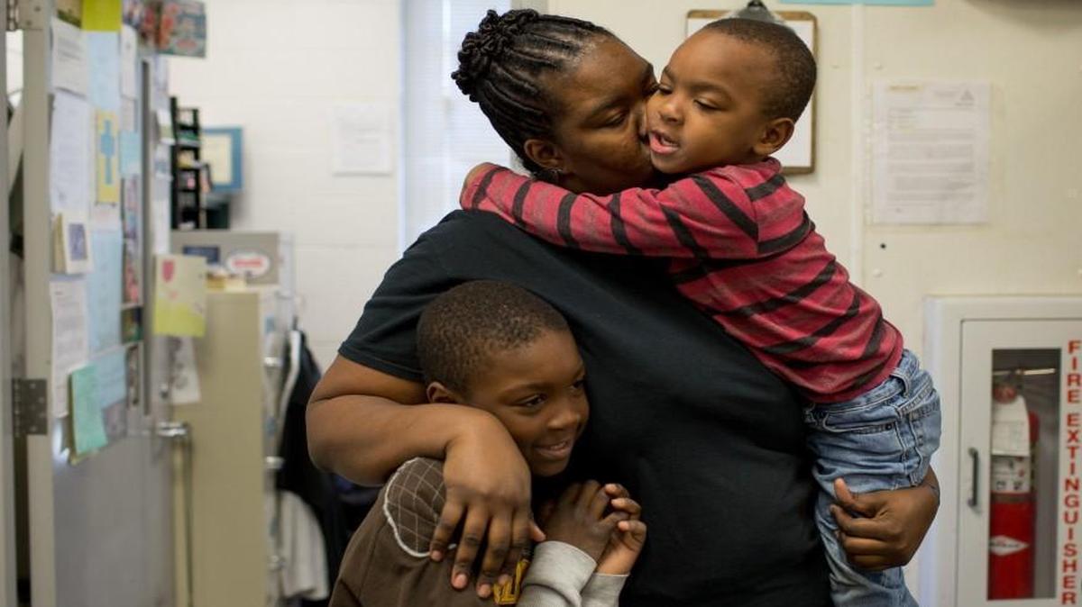 Deanna Nelson holds her son Shone, 4, while her oldest son Monteece, 9, rests against her at the South Wilmington Street Center in Raleigh. The three went to the center to volunteer to feed Thanksgiving dinner to homeless men.