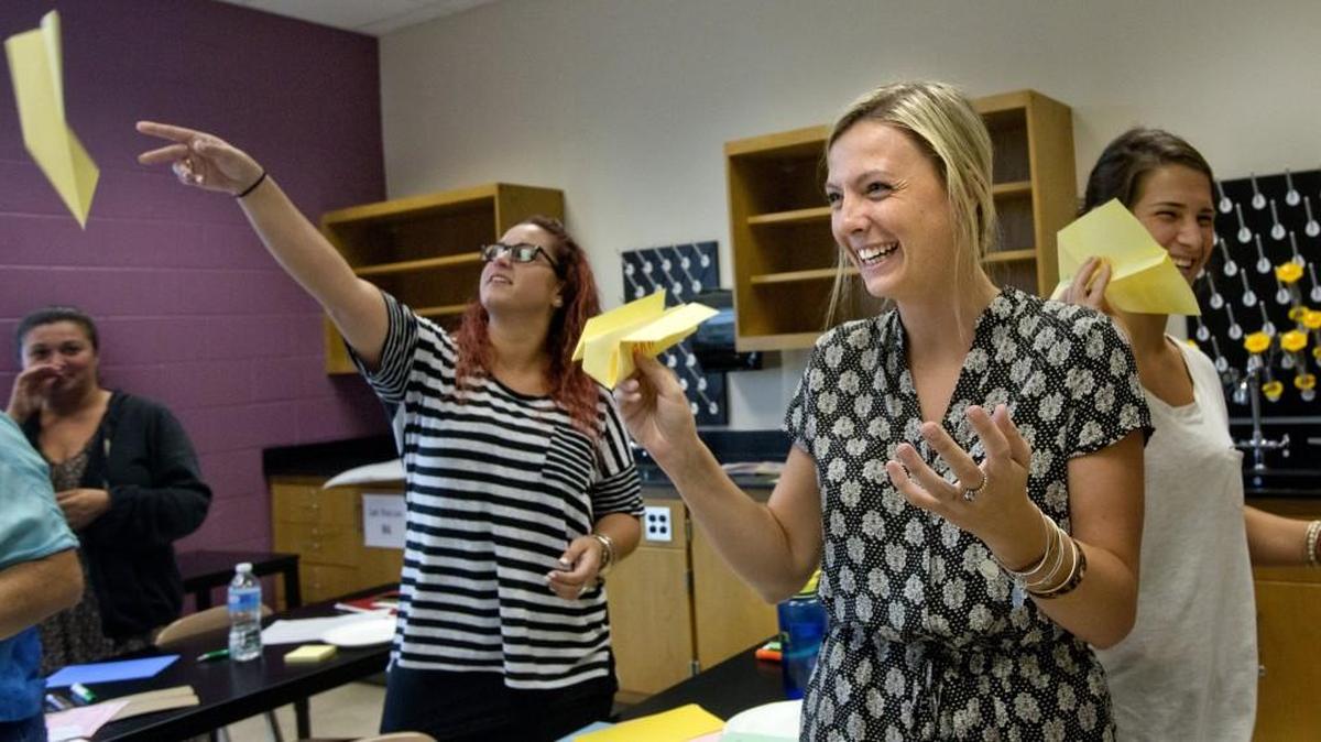 Sending out messages of why they got into teaching, first year educators (from left) Nicole Rindos, Kaitlin Murphy, and Samantha Morakis fly paper airplanes to one another as part of a class exercise in this 2015 Wake County symposium for beginning teachers. North Carolina has historically been backlogged processing teacher licensure applications.