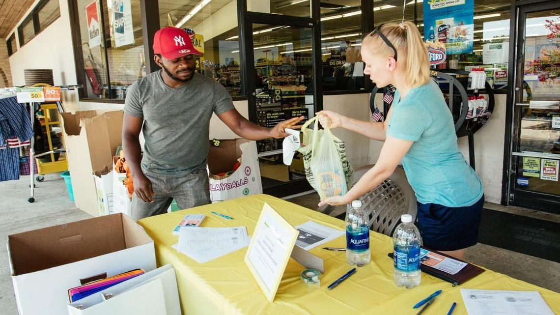 Ola Samuel hands a bag of school supplies to Jillian Knight, a volunteer for Raleigh Rescue Mission, outside Dollar General in Raleigh on July 22.