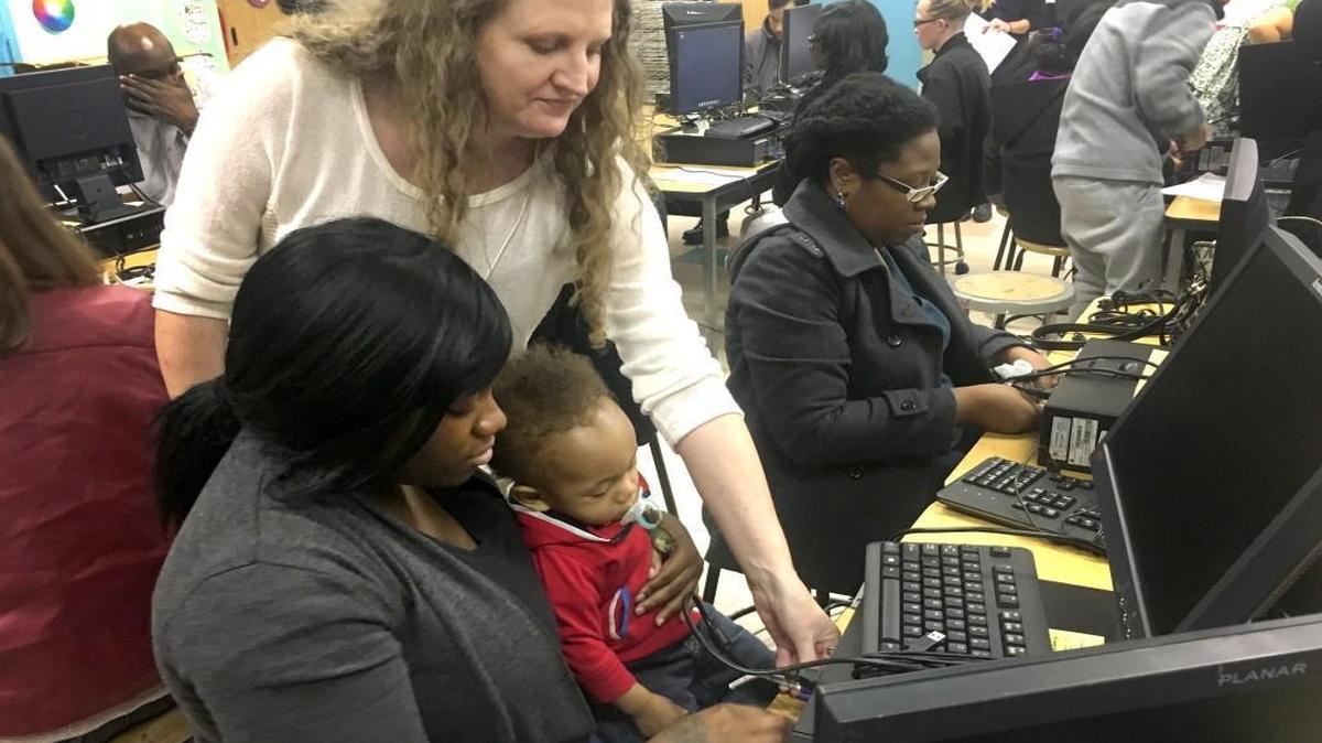 School social worker Johanna Koszegi helps Shantel Mellon, holding 11-month-old son Alvon, hook up her new computer at Hodge Road Elementary School in Knightdale on Nov. 10, 2016.