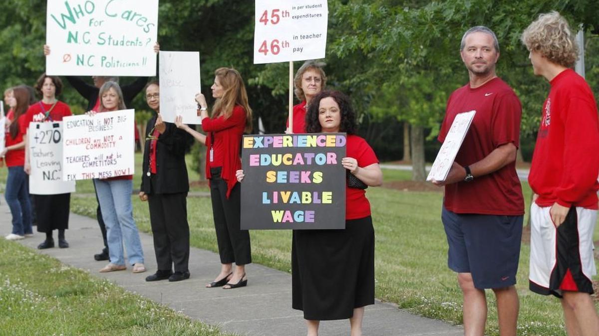 Teachers, including Kristin VanBuskirk, center, a math teacher at Apex High School, rally against high turnover and low pay on the sidewalk in front of Apex High School Wednesday morning, May 21, 2014.