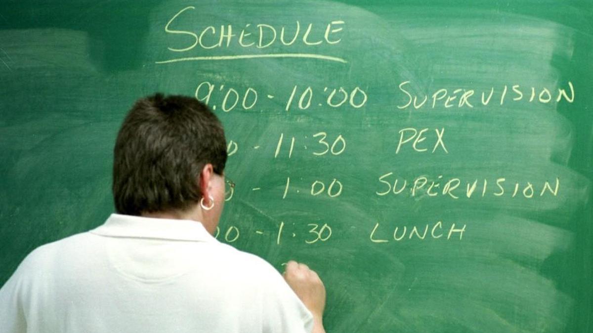 A teacher writes the schedule for the day on her blackboard.