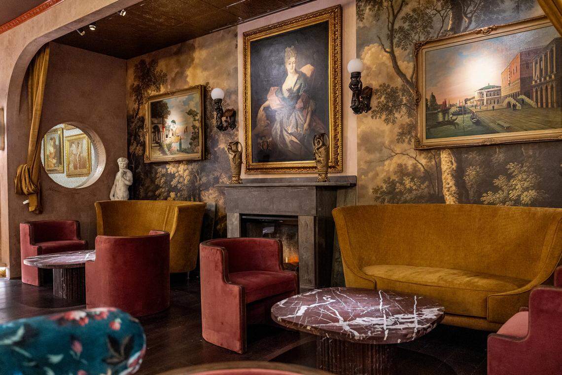 Paintings of Italian landscapes hang above Italian sofas and barrel chairs made with textural velvet fabrics at Capulet Cocktail Club. Tucked into the corners of the room are “confessional booths,” which can be closed off with curtains and feature screens embedded in circular cutouts in the wall.