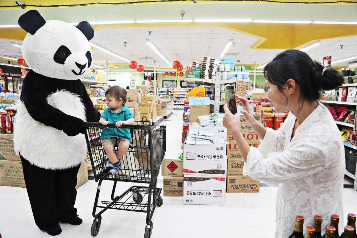 Xinxin Xiao, right, takes a photo of her 17-month-old son, Jettin Lawson, center, with Cydney Graham dressed as a panda, at the A&C Supermarket in Garner on Feb. 21, 2018. Xiao, who travels from Smithfield to shop in the grocery, was delighted to spot the panda, who was in the store by chance with her boyfriend, Bryan Regan, to shoot photos for their Instagram art project, Sideshow Panda.