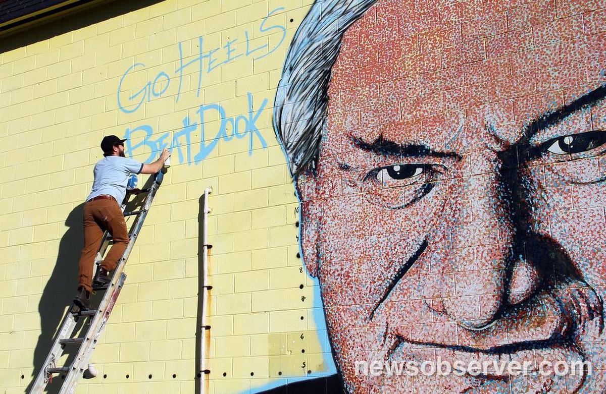 Painter Scott Nurkin works on a larger-than-life mural of larger-than-life UNC coach Dean Smith on a building at Smith Level Road and U.S. 15-501 on the Orange-Chatham county line Saturday, March 7, 2015. Nurkin added a temporary “Go Heels Beat Duke” before planning to paint the yellow background Carolina blue; alas the Blue Devils beat the Tar Heels 84-77.