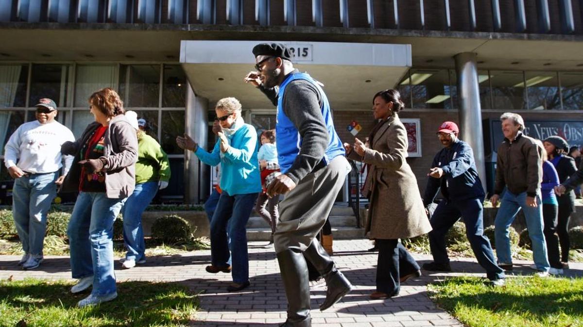 News & Observer columnist Barry Saunders, clad in a Duke Blue Devils jersey, dances the Electric Slide with about 30 fans who jumped in from the crowd in front of The News & Observer building. Saunders agreed to dance if readers donated at least $10,000 to local charities registered in The N&O's Holiday Giving Guide. Readers donated $43,614. In addition to the jersey of his, um, favorite team, Saunders donned a beret and black, knee-high riding boots. The jersey was auctioned for $100, which was given to the Emily Krzyzewski Center in Durham.