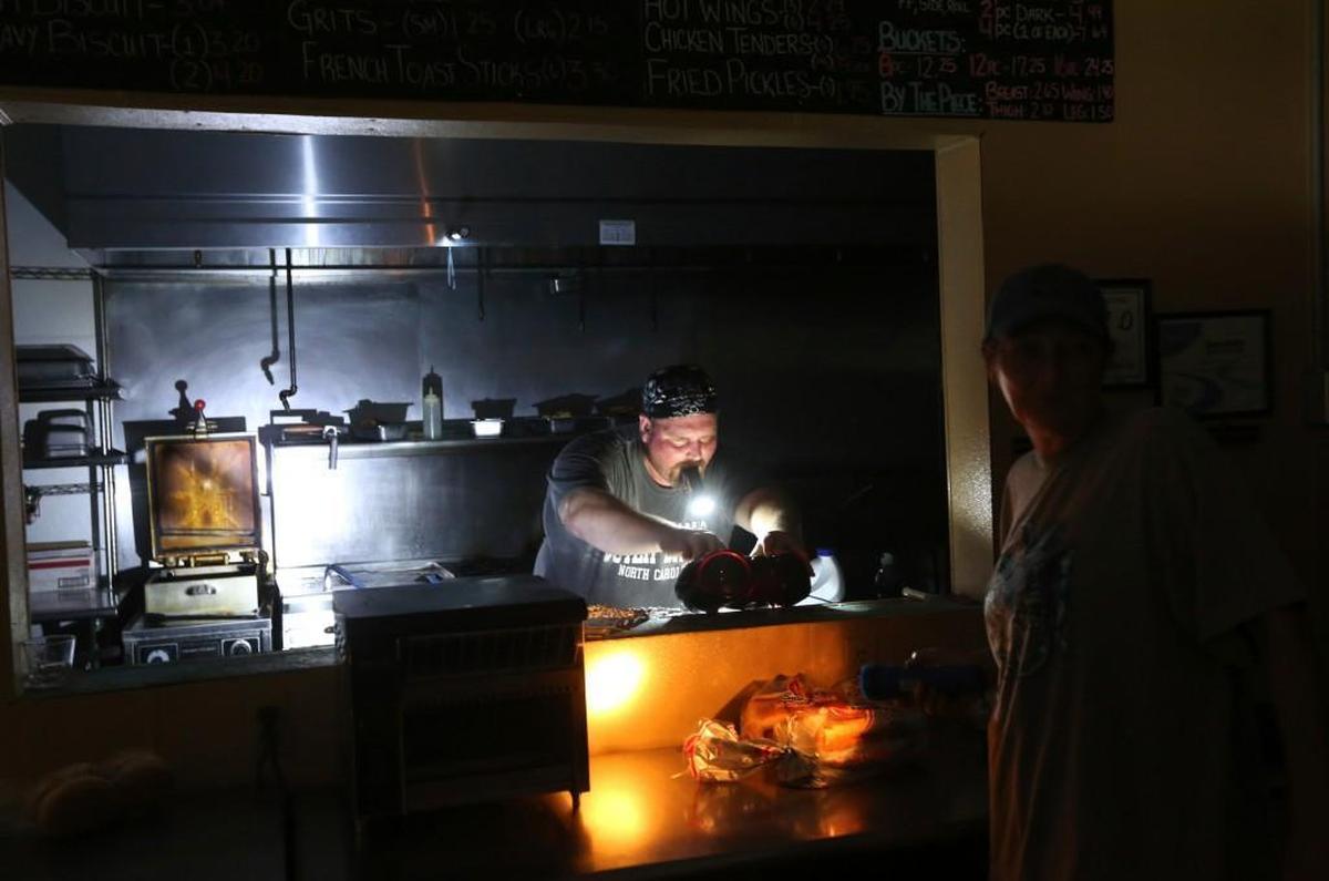Aaron Howe cooks in the dark kitchen at the Island Convenience Store in Rodanthe on Hatteras Island, N.C., on Friday, July 28, 2017. An estimated 10,000 tourists face a noon deadline Friday for evacuating the island on North Carolina's Outer Banks after a construction company caused a power outage, leaving people searching for a place to eat, stay cool or to resume interrupted vacations. Howe says it is the only place in town to get a meal.