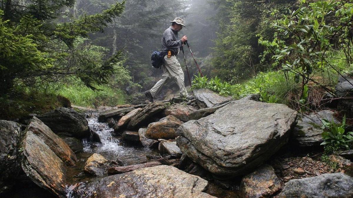 A hiker crosses a stream while hiking the Mountains-to-Sea Trail in Mount Mitchell State Park.
