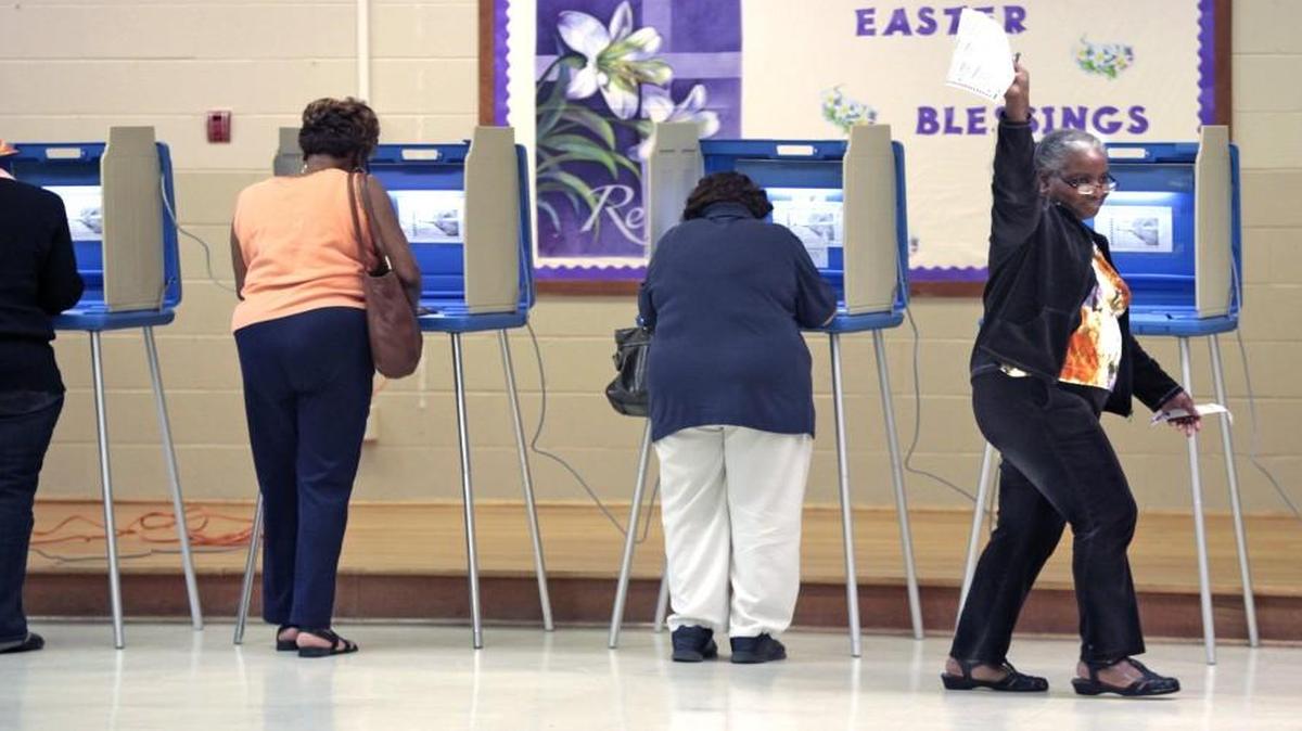 At right, a voter waves her completed ballot to a poll worker as she moves toward the vote counting machine at the White Rock Baptist Church precinct on Fayetteville Road, Durham, NC Tuesday, March 15, 2016.