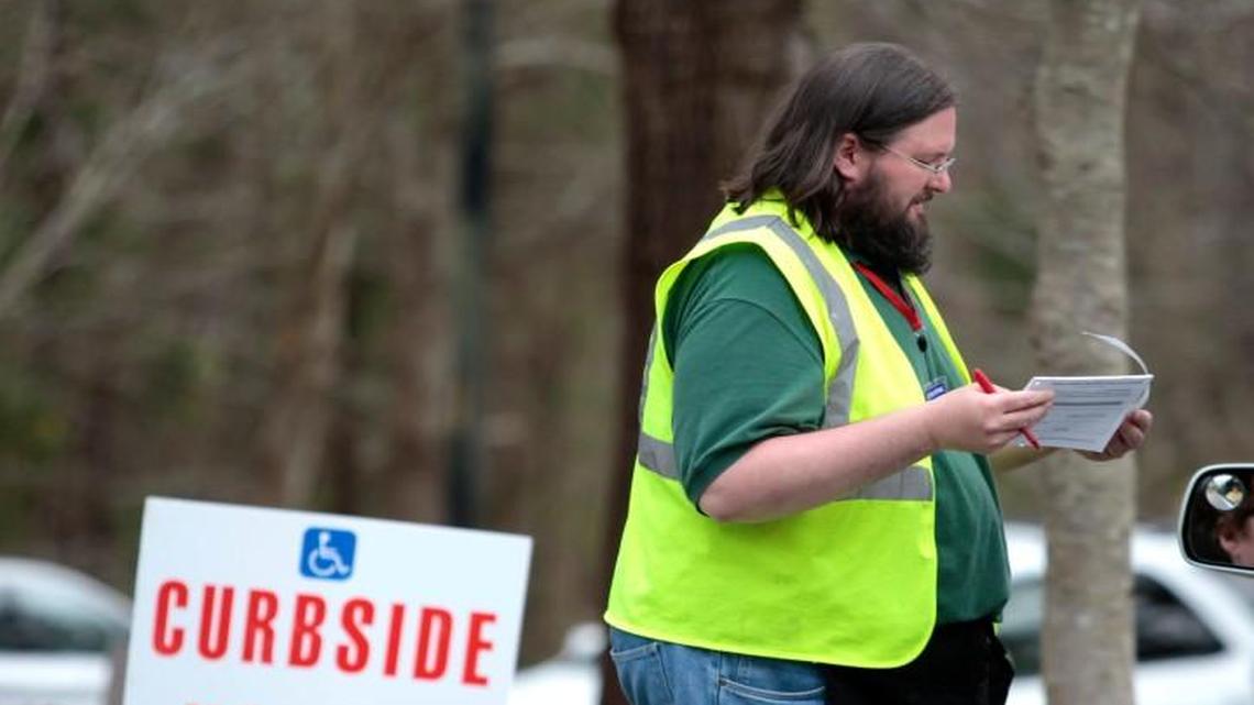 Wake County poll worker John Banker helps a curbside voter with her paperwork outside of the early voting site at the Lake Lynn Community Center in North Raleigh on March 11, 2016.