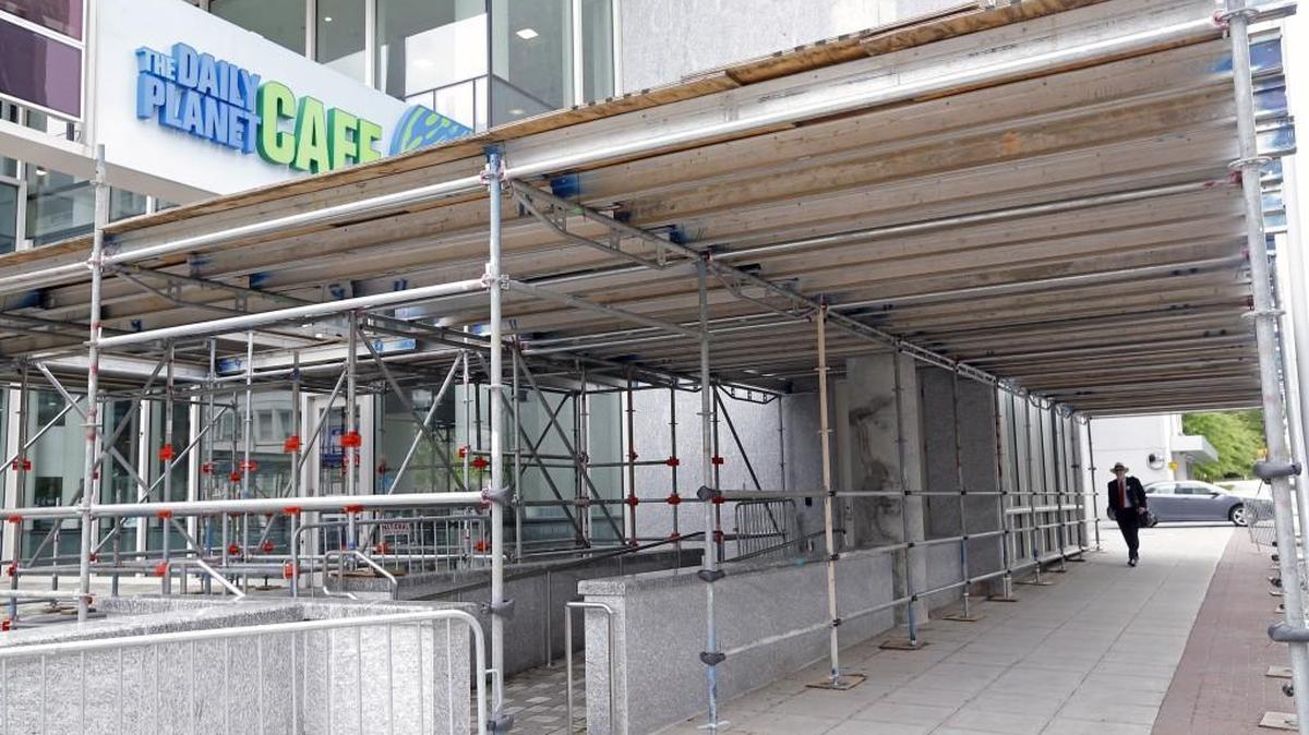 A pedestrian walks down a sidewalk covered by a scaffold near the Daily Planet Cafe in the Museum of Natural Sciences Nature Research Center Building in Raleigh on April 20, 2015. Debris has fallen off this building and also off the adjacent State Employees Credit Union Building and the scaffolds protect people below from falling objects.