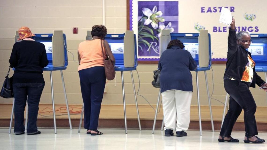 At right, a voter waves her completed ballot to a poll worker as she moves toward the vote counting machine at the White Rock Baptist Church precinct on Fayetteville Road, Durham, NC Tuesday, March 15, 2016.