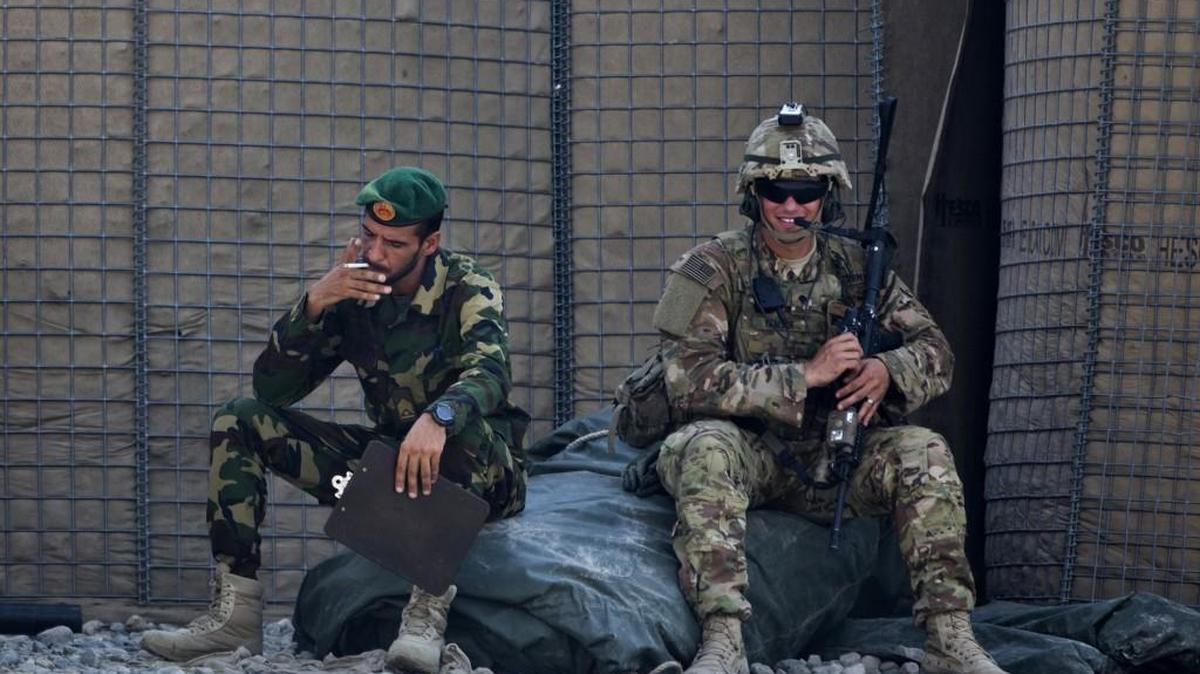 FILE - In this Wednesday, Aug. 5, 2015 file photo, an Afghan National Army soldier, left, smokes as a U.S. Army soldier from Charlie Company, 2-14 Infantry Regiment, 2nd Brigade, 10th Mountain Division sits next to him in Camp Khogyani in Nangarhar province, east of Kabul, Afghanistan.