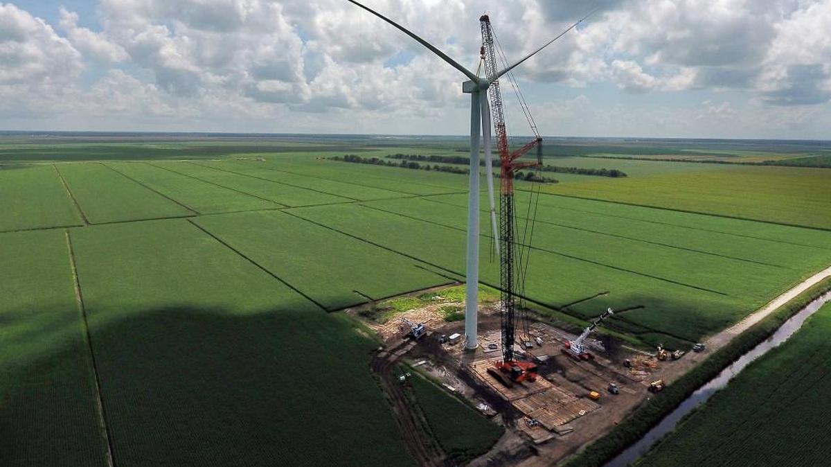A large crane holds the blade assembly as a wind turbine tower is constructed in August near Elizabeth City.