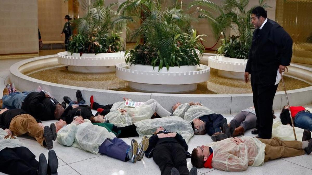 Rev. William Barber, head of the NC NAACP, standing, prays over 13 protesters who participated in a die-in at under the rotunda of the NC Legislature in February 2015 to protest the state’s continued denial of Medicaid expansion for hundreds of thousands of North Carolinians. The protesters were from the NC NAACP and the Forward Together Moral Movement.