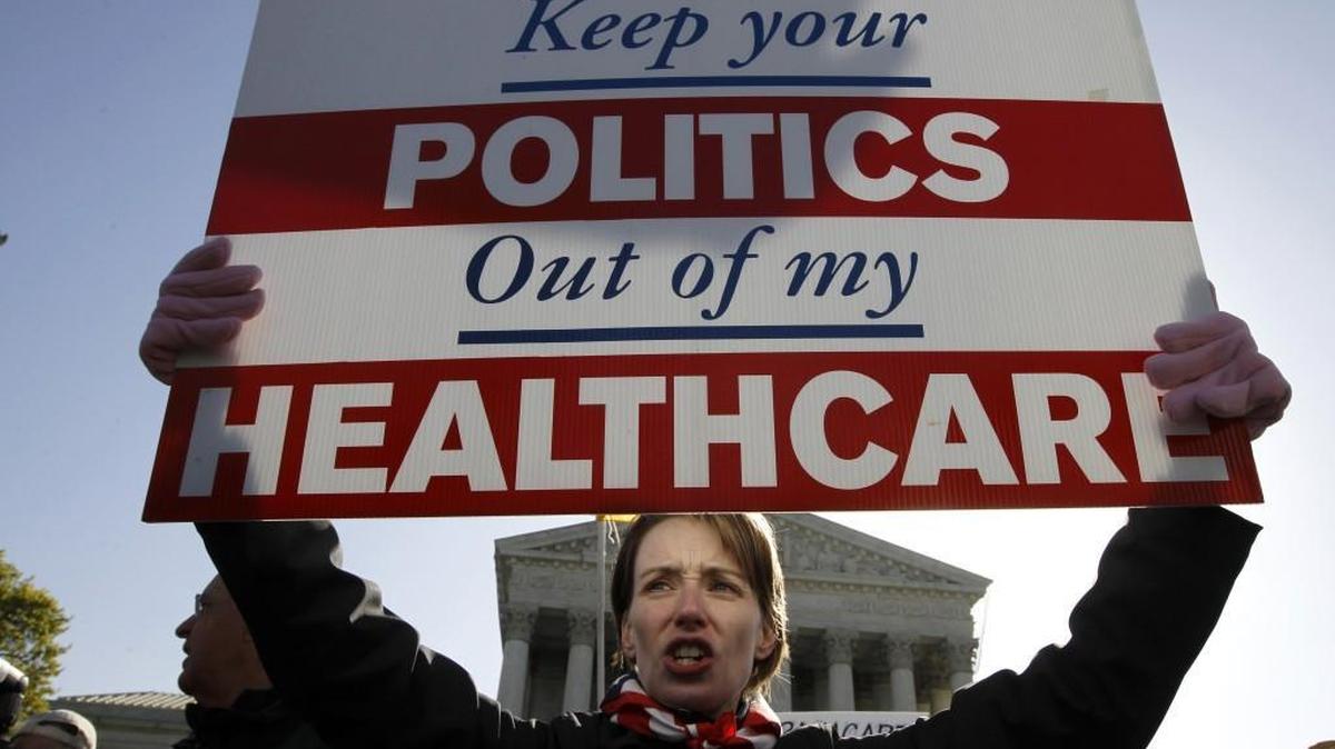 FILE - In this Tuesday, March 27, 2012 file photo, Amy Brighton from Medina, Ohio, who opposes health care reform, holds a sign in front of the Supreme Court in Washington during a rally as the court continues arguments on the health care law signed by President Barack Obama. Entrenched political divisions over "Obamacare" have driven most Republican-led states to turn their backs on the biggest expansion of the social safety net in a half century. (AP Photo/Charles Dharapak)