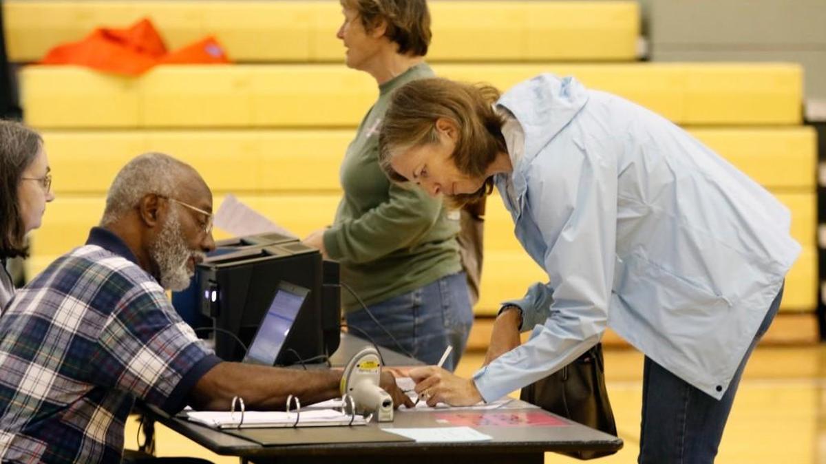 Chapel Hill High School/North Carrboro precinct worker Braxton Foushee, left, helps a voter do the paperwork to get her ballot before she voted in the school gym November 3 in the Orange County municipal elections also with voting for school board offices and five bond referendums. 2016 brings the official start of North Carolina’s new voter ID requirements, which will be in place for the March 15 primary.