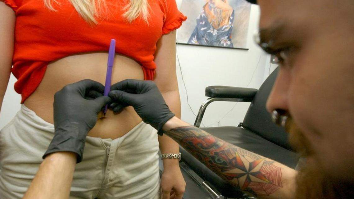 Matt Cousins marks Charlotte Pipkin's belly button before piercing her at Warlocks Piercings and Tattoos in Raleigh.