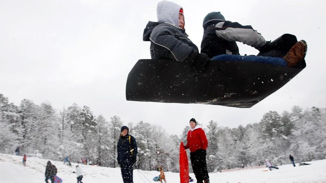 Sledders go airborne after piloting their mat over a ramp made of packed snow at Bond Park in Cary in December 2010.