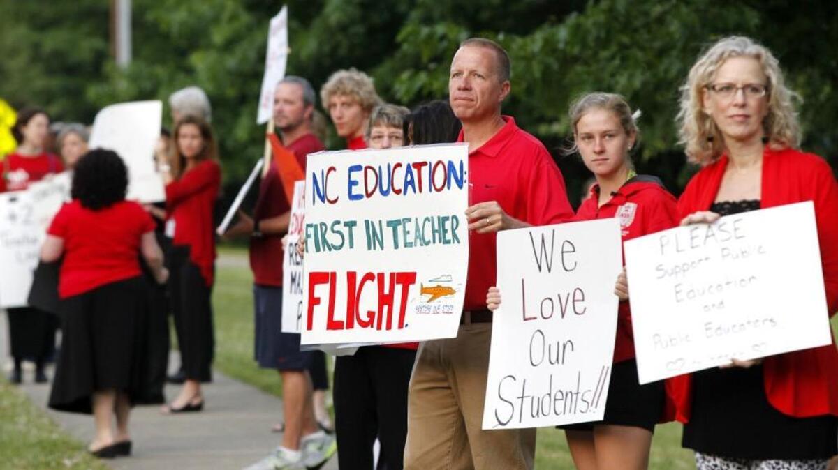 Scott Ferguson, center, an English teacher at Apex High School, rallies with fellow teachers and supporters against high turnover and low pay of teachers on the sidewalk in front of Apex High School on May 21, 2014. A bill proposed by state Sen. Ralph Hise (R-Mitchell County) would eliminate state payroll deductions for dues to employee groups such as the NC Association of Educators, which lobbies for better teacher pay.