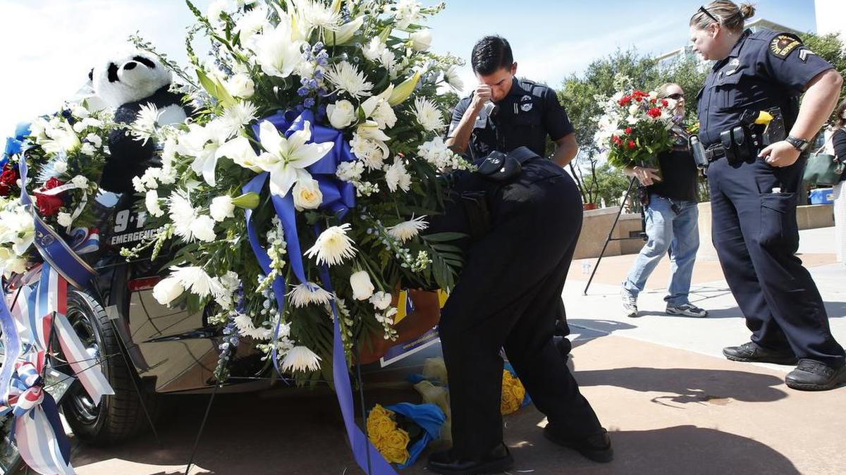A Dallas Police officer wipes a tear as fellow officers adjust flowers left on a police cruiser in from of Police Headquarters in Dallas on Friday, July 8, 2016, following the fatal sniper attack on Thursday.