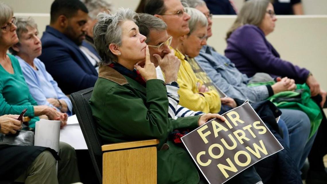 Attendees hold signs as they listen to discussions at a joint House - Senate committee meeting on judicial reform and redistricting held at the Legislative Office Building in downtown Raleigh on Jan. 22, 2018.