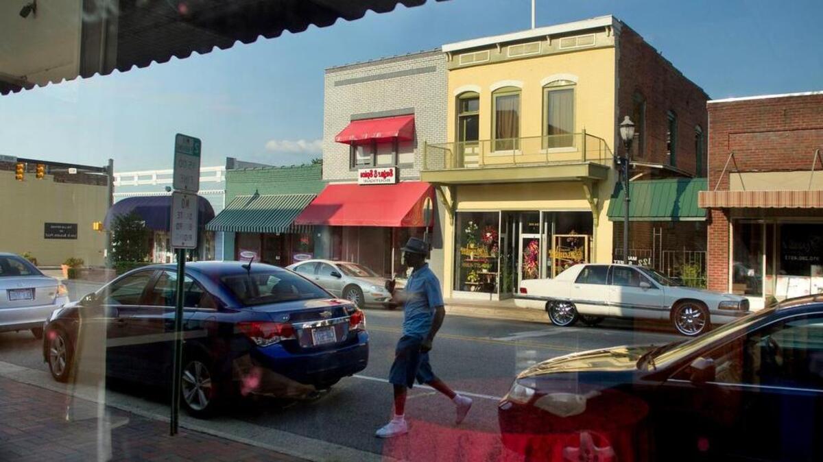 
Pernell Carthens is reflected in a shop window as he steps across Main Street on Friday, July 24, 2015 in Laurinburg, N.C. after talking with a friend. Carthens is reflected in a window of a vacant business along the once vibrant street. The Laurinburg Downtown Revitalization Corp. has invested $165,000 to freshen up the store fronts downtown. After power washing and fresh paint, new awnings were installed.
