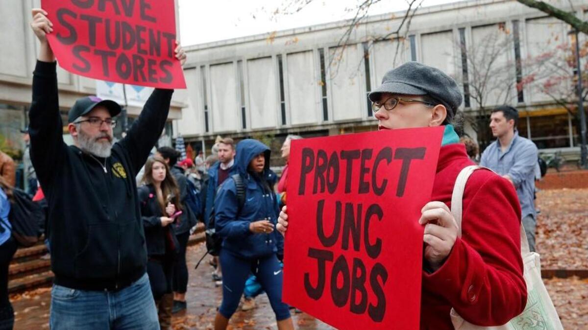 Jason Adams, left, and Christina Pelech hold signs as a rally is held at the Student Stores on the UNC campus on Monday to protest a proposal to privatize the operation of the store. Both previously worked in the Bull's Head Bookstore, a section within the larger student store. About 100 people came to the rally.