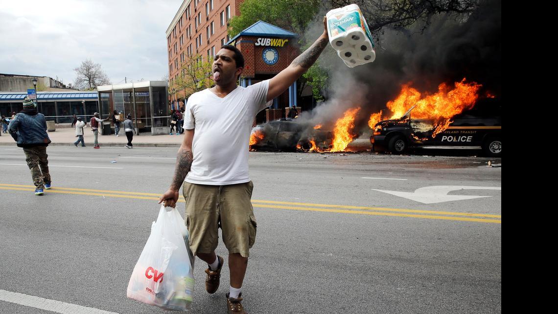 
A man carries items from a store as police vehicles burn after the funeral of Freddie Gray in Baltimore. 
