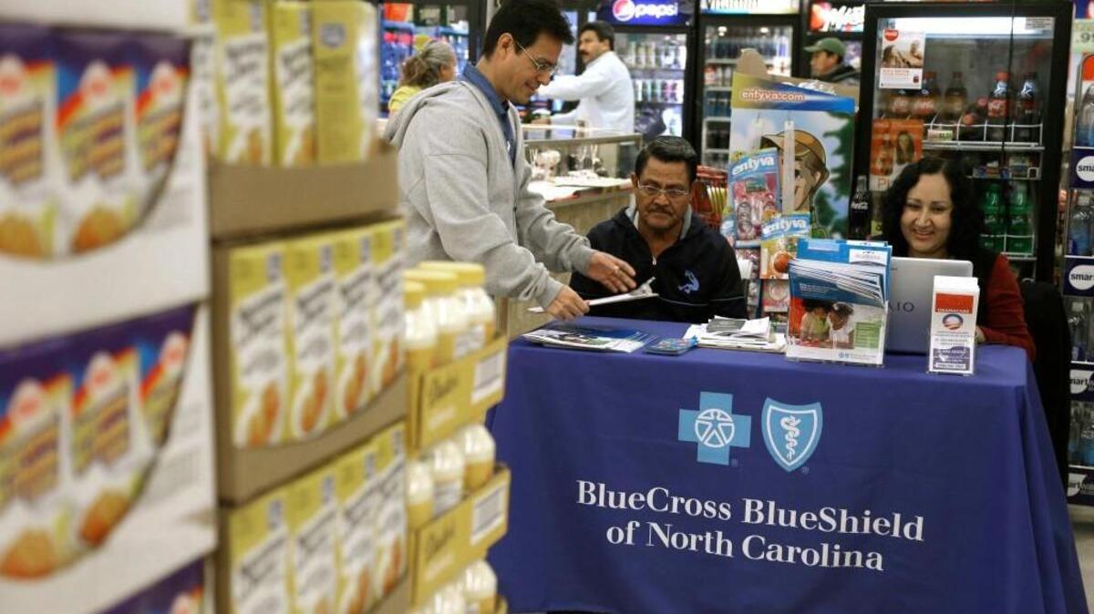 In this file photo taken Nov. 22, 2014, Blue Bridge Benefits LLC agent Patricia Sarabia, right, and Adolfo Briceno, left, with Spanish Speaking LLC, help a potential customer with Blue Cross Blue Shield at a kiosk promoting Obama Care at Compare Foods in Winston-Salem, N.C.