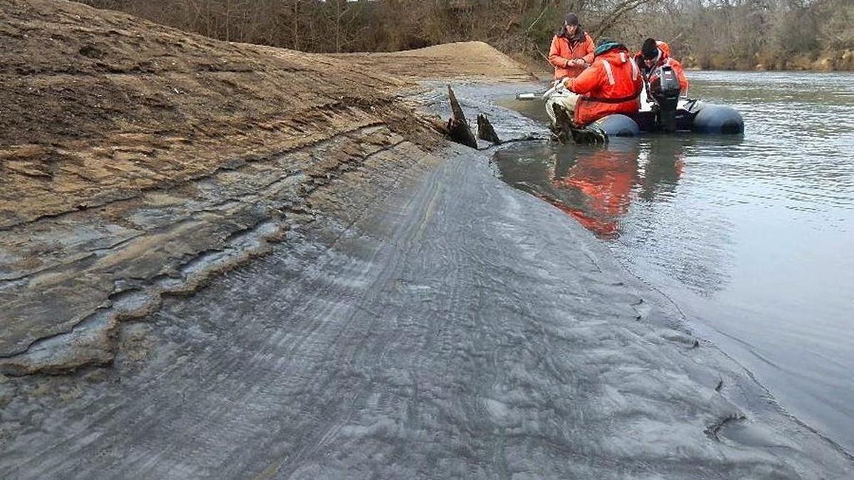 In February 2015, Tom Augspurger, left, with the USFWS, takes a core sample during a reconnaissance of the Dan River coal ash spill. John Fridell of the USFWS and Rick Smith of Duke Energy are with him.